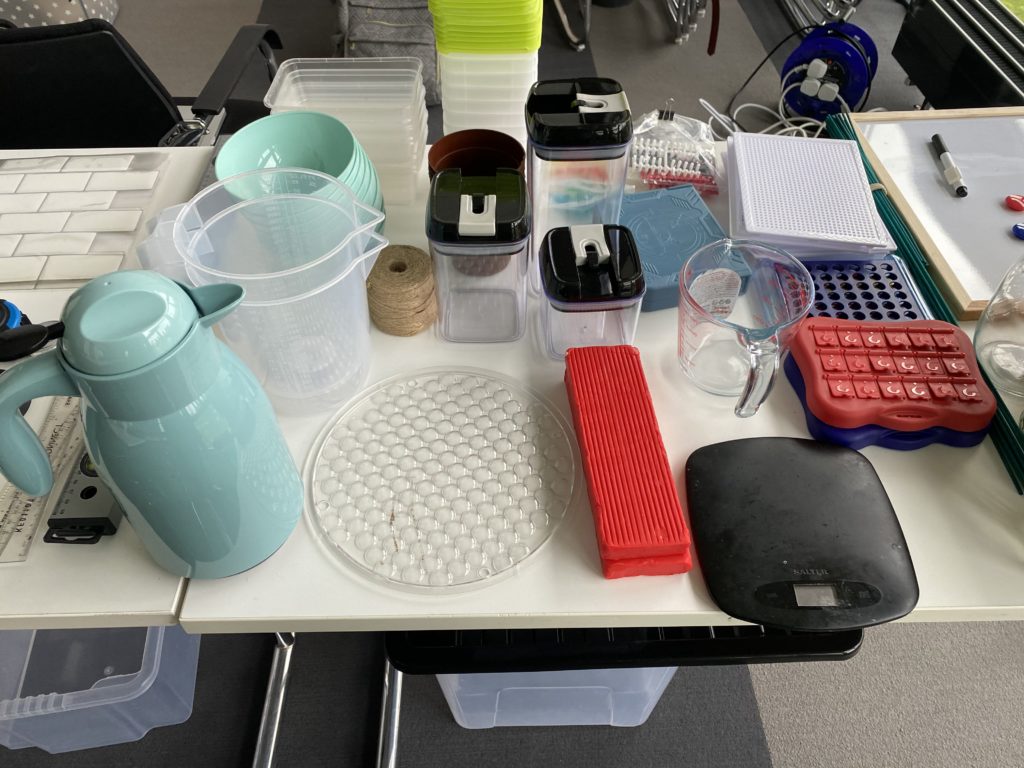 Sets of bottle, measuring jugs, cups, and other kitchen containers are laid out on a table